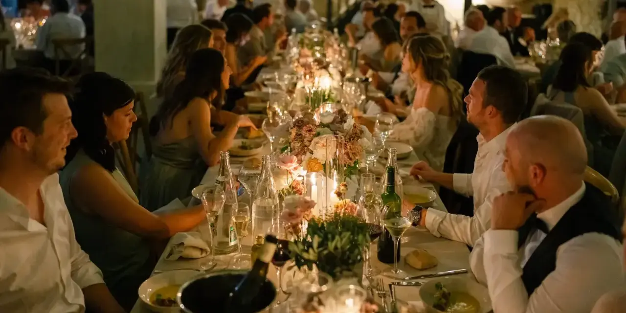 Un dîner de mariage réussi, avec une longue table dressée, des bougies, des fleurs et des invités souriants.