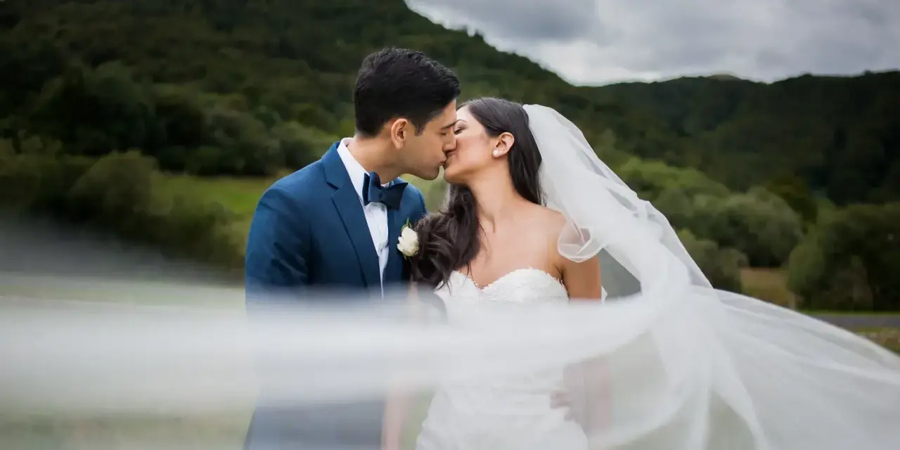 Un couple s'embrasse, le voile de la mariée flottant au vent. Une scène romantique qui donne envie de savoir comment organiser un mariage.