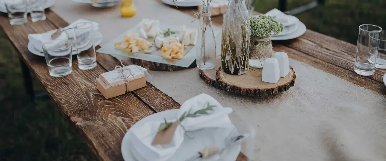 Table setting rustique pour une préparation de cérémonie laïque : assiettes, verres, plateau de fromages, cadeaux et décoration florale.