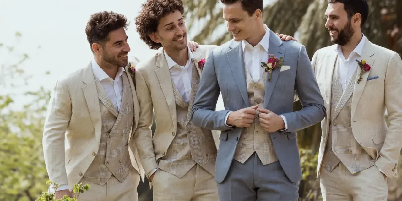 Quatre hommes en costumes de lin, dont un témoin et un garçon d'honneur, sourient et discutent à l'extérieur.