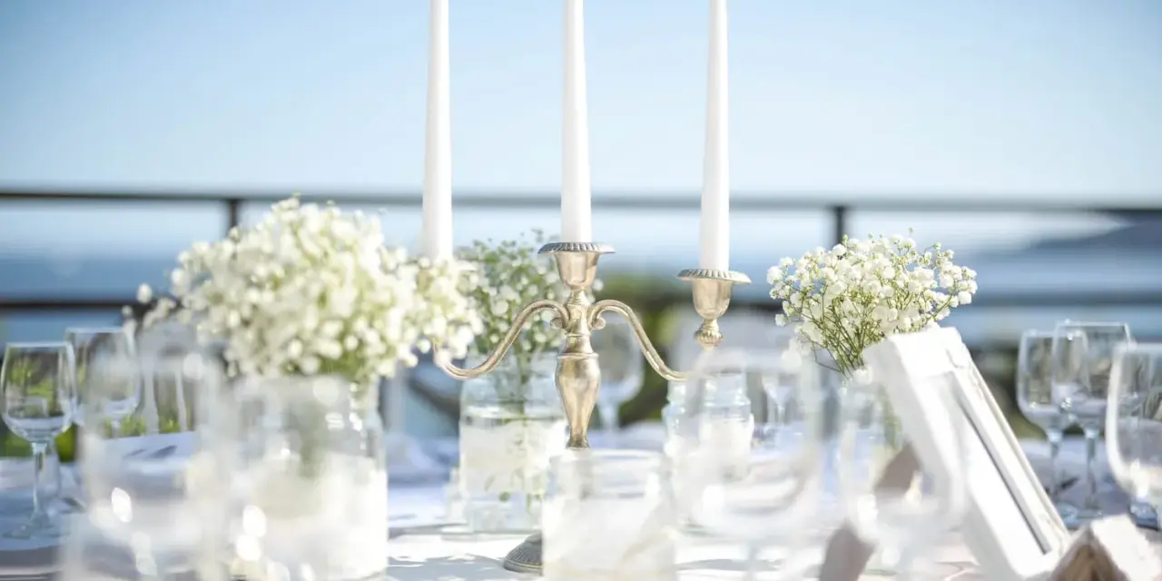 Décoration de mariage : bougies, fleurs et verres sur une table. La distance entre 2 tables mariage est suggérée par l'agencement.