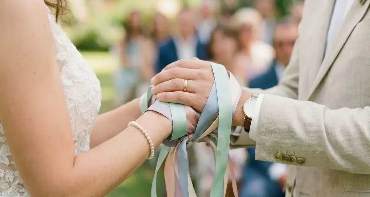 Mains jointes, rubans pastel noués, symbole d'un rituel d'union. Le couple célèbre son amour.