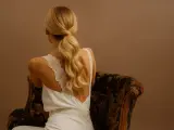 Une invitée de mariage arbore une élégante robe blanche et une queue de cheval blonde, assise sur un fauteuil fleuri.