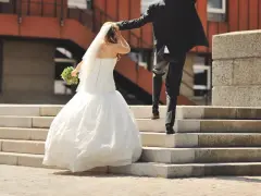 Un couple s'enfuit sur des escaliers après leur cérémonie de mariage. La mariée porte une robe blanche et un voile, tenant un bouquet.