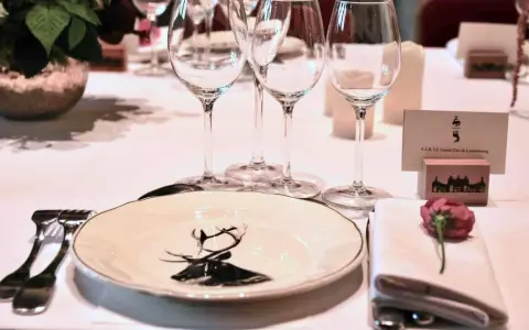 Une élégante table de mariage dressée avec des verres à pied, une assiette ornée d'un cerf, et un marque-place pour le Grand-Duc de Luxembourg.