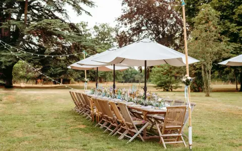 Table dressée pour un mariage jardin, avec des chaises en bois, des parasols et des guirlandes lumineuses.