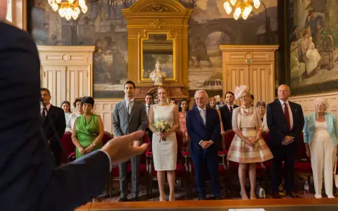 Le couple se tient au centre, entouré de leurs 5 témoins mariage. La mariée porte une robe blanche et tient un bouquet. Les invités sont élégamment vêtus.