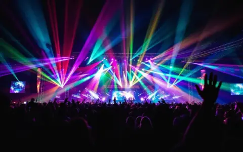 Une foule en délire sous un **totem jeux de lumière** spectaculaire, des faisceaux multicolores illuminent la scène et le public.