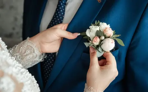 Les mains délicates de la mariée ajustent la boutonnière sur le costume bleu du marié, un symbole de leur mariage avec un étranger.