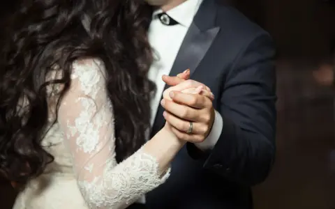 Les mains jointes d'un couple dansant une valse mariage. La mariée porte une robe en dentelle, le marié un costume sombre.