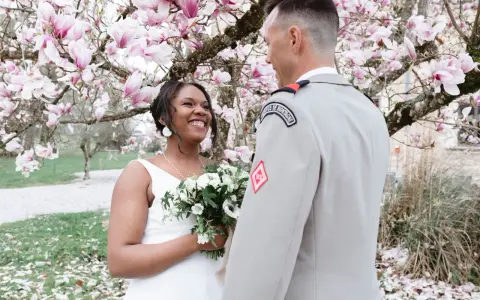 Un couple rayonnant lors de leur mariage militaire, sous un magnolia en fleurs.