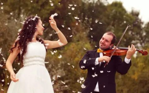 Une mariée en robe blanche danse sous une pluie de plumes, tandis que son mari joue du violon. Une scène féerique pour un mariage champêtre.