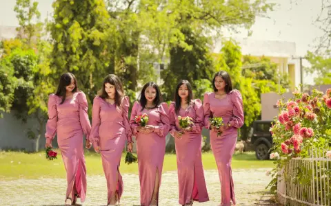 Cinq demoiselles d'honneur en robes roses marchent ensemble, tenant des bouquets.