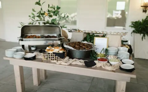 Buffet de brunch mariage avec plats chauds, petits pains, garnitures et assiettes empilées.