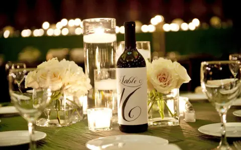 Bouteille de vin avec étiquette "Table 16", entourée de roses pâles, bougies et verres à vin. Parfait pour un dîner avec droit de bouchon traiteur.