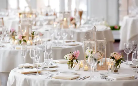 Un élégant plan de table mariage en U, avec des tables rondes dressées de vaisselle fine, de verres à pied, de bougies et de bouquets de roses.