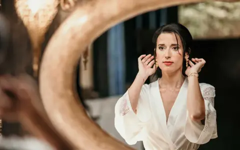 Une mariée, le visage marqué par le stress du mariage, ajuste ses boucles d'oreilles devant un miroir.
