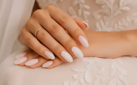 Mains d'une mariée avec des ongles tendance, ornés d'une bague dorée et d'un motif floral délicat sur un ongle.