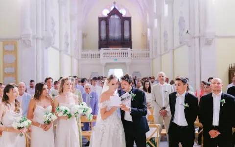 Mariage dans une église : la mariée et le marié lisent un texte, entourés des invités et des demoiselles d'honneur.