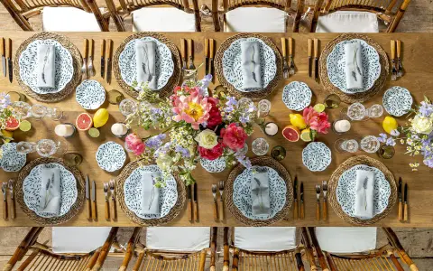 Plan de salle mariage table ronde : une table en bois dressée avec des assiettes fleuries, des verres en cristal, des fruits et des bouquets de fleurs.