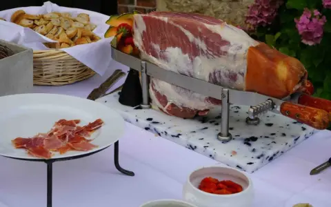 Un jambon cru entier prêt à être découpé, accompagné de pain et de fruits, pour un vin d'honneur original.