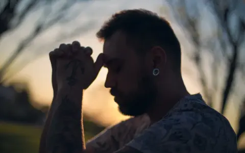 Un homme aux mains jointes, le front appuyé sur ses doigts, semble en pleine prière. Son tatouage d'ancre est visible. C'est un moment de prière des époux.