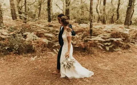 Un couple se promène dans une forêt, la mariée porte une robe blanche et tient un bouquet. Une scène de formalité mariage en pleine nature.