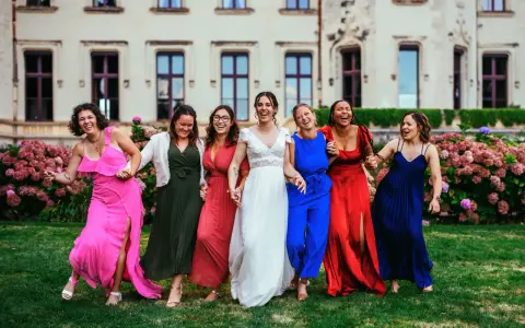 Un groupe de femmes rit joyeusement devant un château. La mariée en blanc est entourée de ses demoiselles d'honneur en robes colorées. La différence entre témoin et demoiselle d'honneur est subtile, mais leur complicité est évidente.