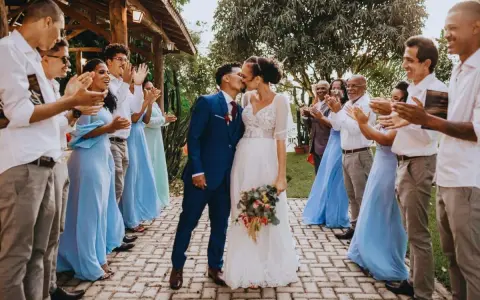 Un couple s'embrasse lors de leur petit mariage de 20 personnes. Les invités, en tenues bleues et blanches, applaudissent joyeusement.