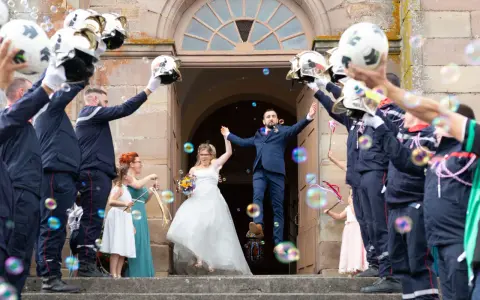 Mariés sortant de l'église sous une haie d'honneur mariage de pompiers lançant des bulles.