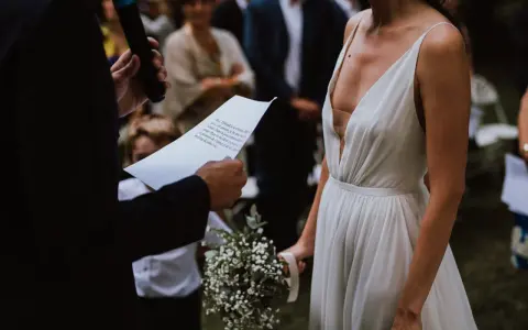La mariée en robe blanche, bouquet à la main, écoute les vœux lors de son mariage religieux.