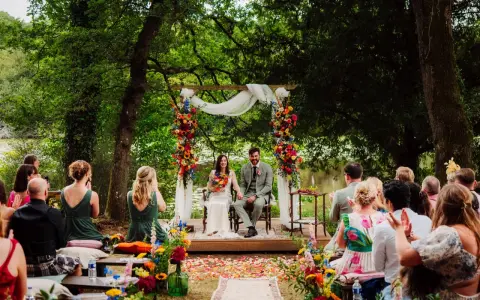 Un couple souriant lors d'une cérémonie laïque en plein air, entouré de verdure et de fleurs colorées. L'officiant cérémonie laïque guide ce moment unique.