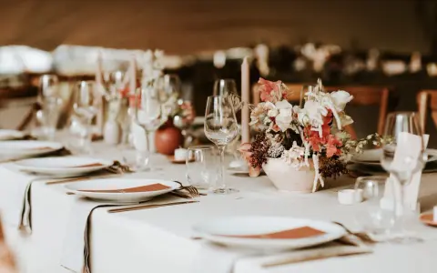 Un plan de table mariage élégant : vaisselle, verres, bougies et un bouquet de fleurs sur une table dressée.