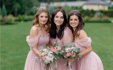 Trois demoiselles d'honneur souriantes en robes roses, tenant des bouquets de fleurs. Une belle scène pour une demande demoiselle d'honneur.