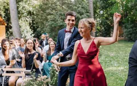 Un couple rayonnant danse lors d'un cortege mariage en plein air. La foule applaudit et filme ce moment joyeux.