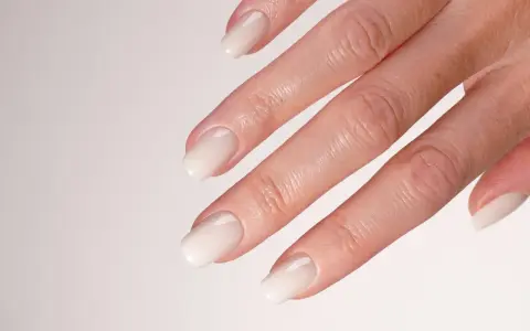 Main d'une mariée avec un french manucure spécial mariage, aux ongles laqués d'un blanc nacré, prêts pour le grand jour.