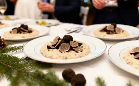 Un délicieux repas mariage hiver : des assiettes de risotto aux truffes noires, garnies de fines lamelles, sur une table dressée avec des branches de sapin.