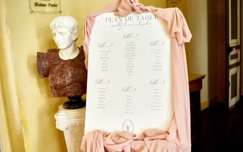 Plan de table de mariage, avec la disposition des invités par table. Une statue antique et des drapés roses décorent l'entrée.