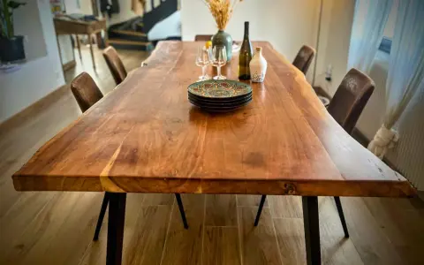 Table rectangulaire en bois massif, prête pour un repas festif dans une salle des fêtes. Assiettes décorées, verres et bouteille attendent les convives.