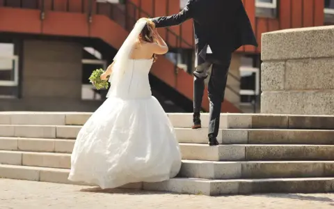 Un couple s'enfuit sur des escaliers après leur cérémonie de mariage. La mariée porte une robe blanche et un voile, tenant un bouquet.