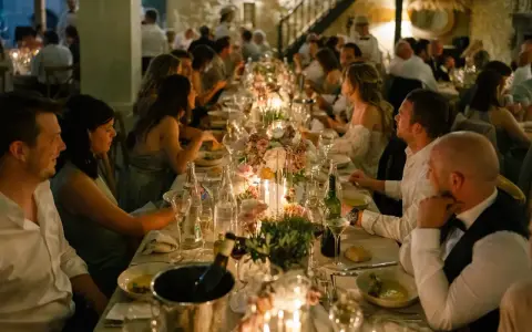 Un dîner de mariage réussi, avec une longue table dressée, des bougies, des fleurs et des invités souriants.