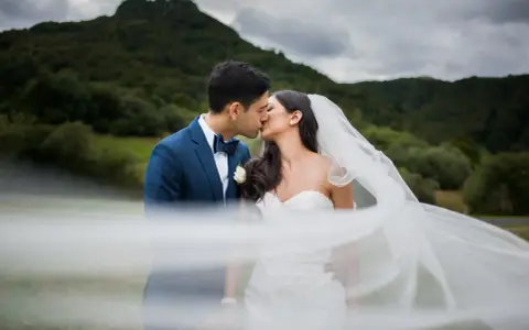 Un couple s'embrasse, le voile de la mariée flottant au vent. Une scène romantique qui donne envie de savoir comment organiser un mariage.