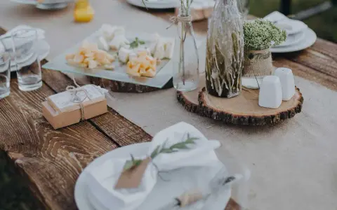 Table setting rustique pour une préparation de cérémonie laïque : assiettes, verres, plateau de fromages, cadeaux et décoration florale.