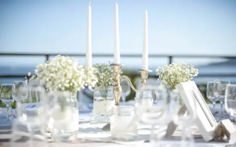 Décoration de mariage : bougies, fleurs et verres sur une table. La distance entre 2 tables mariage est suggérée par l'agencement.