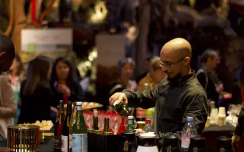 Un barman sert du vin lors d'un vin d'honneur pour 100 personnes. Des bouteilles et des verres sont disposés sur le comptoir.