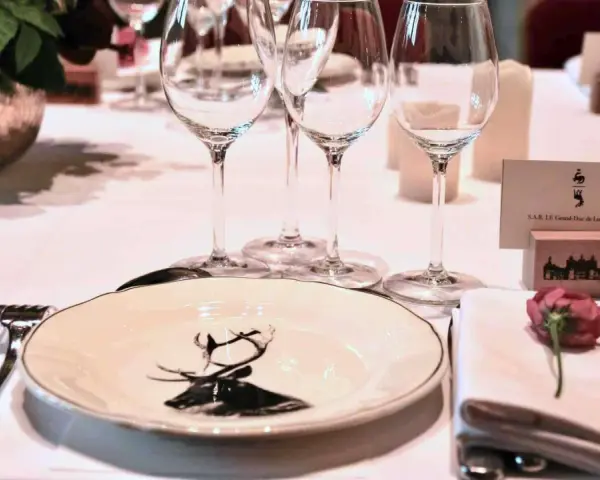 Une élégante table de mariage dressée avec des verres à pied, une assiette ornée d'un cerf, et un marque-place pour le Grand-Duc de Luxembourg.