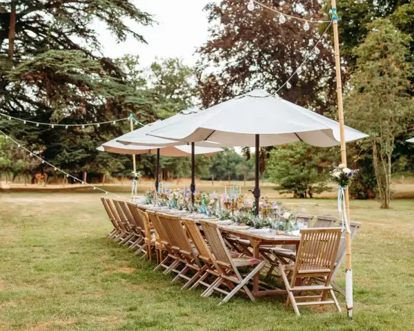 Table dressée pour un mariage jardin, avec des chaises en bois, des parasols et des guirlandes lumineuses.