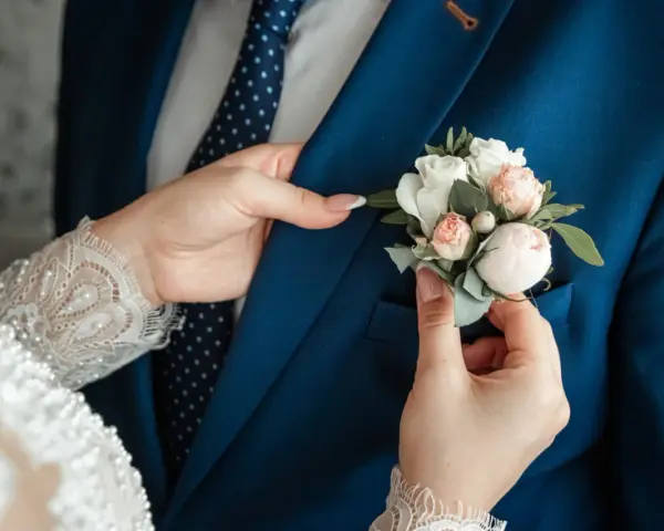 Les mains délicates de la mariée ajustent la boutonnière sur le costume bleu du marié, un symbole de leur mariage avec un étranger.
