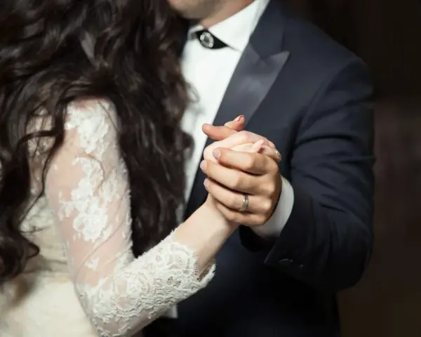 Les mains jointes d'un couple dansant une valse mariage. La mariée porte une robe en dentelle, le marié un costume sombre.