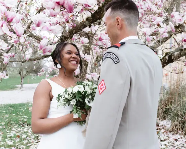 Un couple rayonnant lors de leur mariage militaire, sous un magnolia en fleurs.
